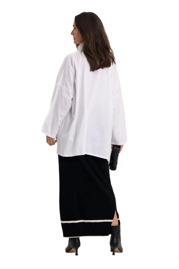 A woman shown from the back wearing an oversized 100% cotton white long-sleeve top and a black maxi skirt with a white stripe at the hem, paired with black ankle boots, against a plain white studio background.
