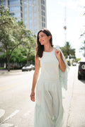 Woman in a light green mint outfit standing on a city street with buildings and trees in the background.