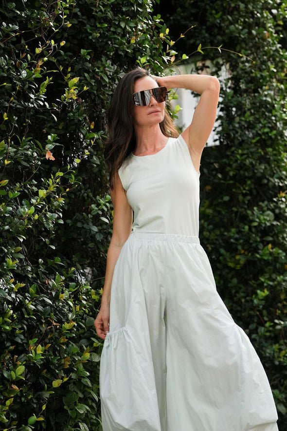 Woman in a mint lycra cotton tank in sunglasses standing against a green leafy wall in Fort Lauderdale.