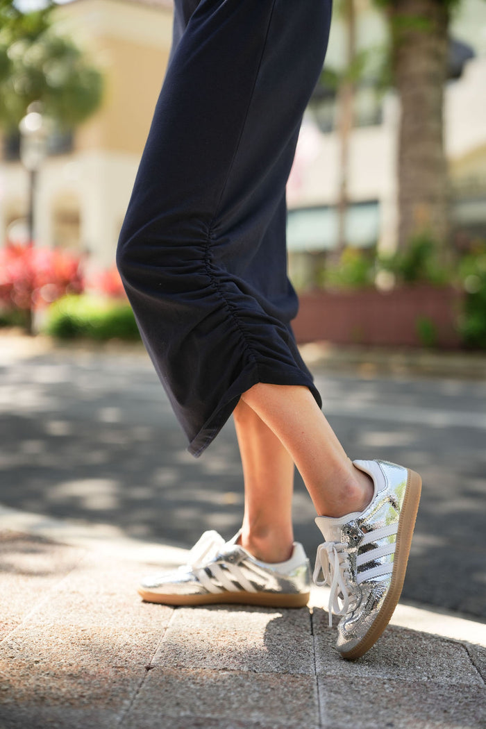 Person wearing silver sneakers and a black ruche lycra cotton dress with a blurred outdoor background