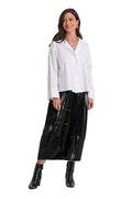 A woman modeling a white 100% cotton long-sleeve button-up shirt and a shiny black midi skirt with black ankle boots, standing against a plain white studio background.