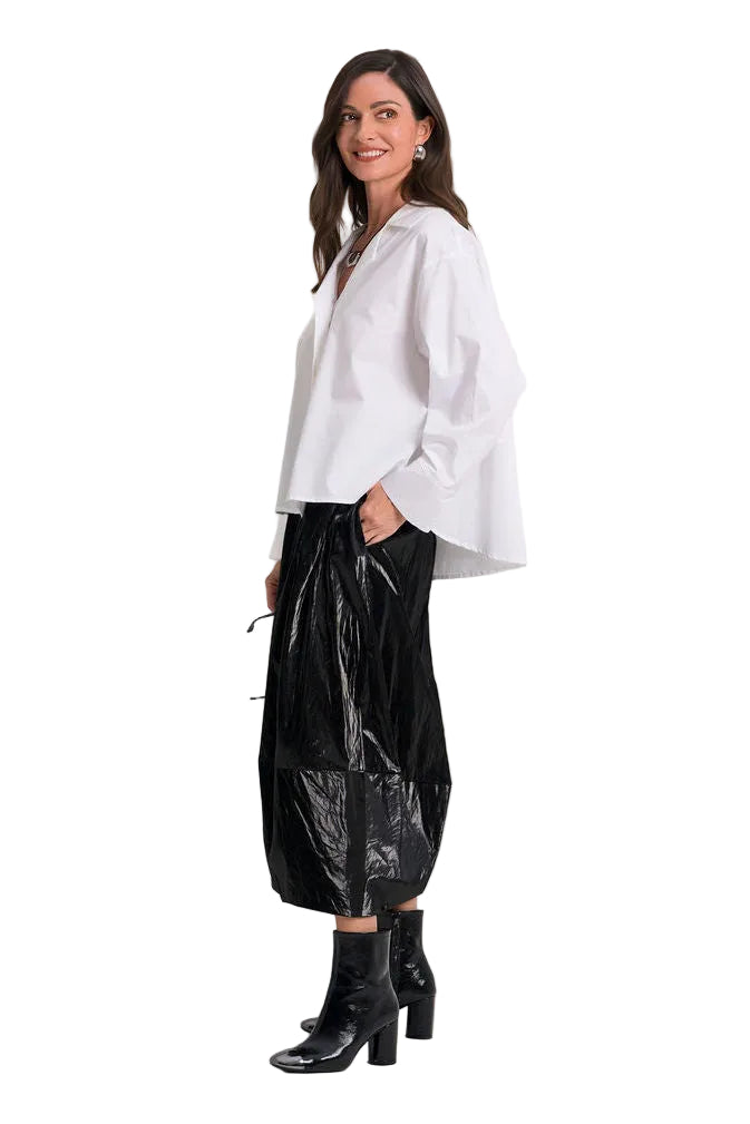 A woman modeling a 100% cotton white long-sleeve blouse and shiny black skirt against a plain white background.
