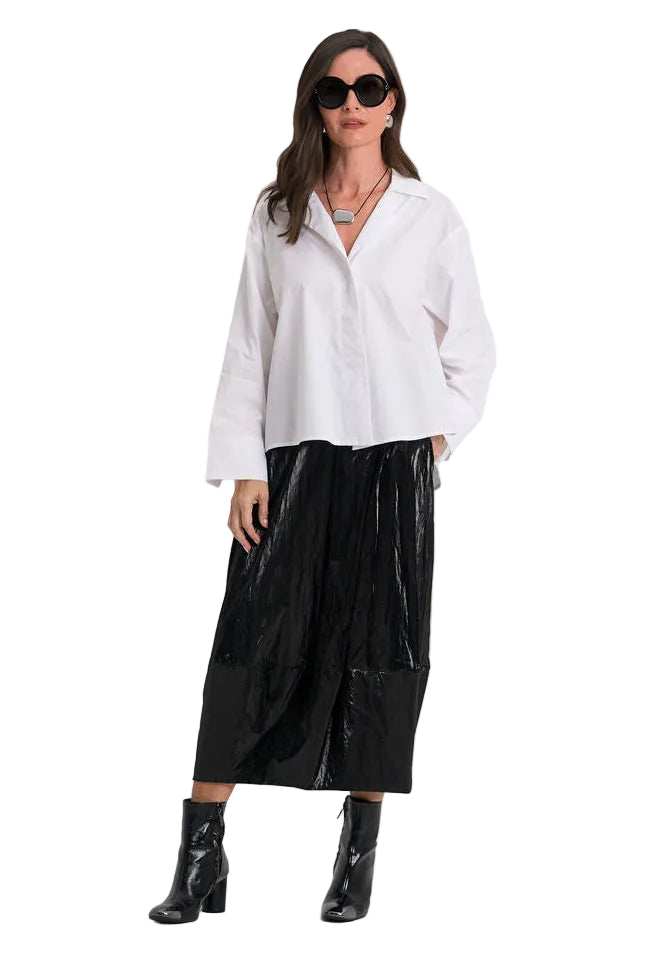 A woman modeling a 100% cotton white long-sleeve button-up shirt and shiny black wide-leg pants with black ankle boots, photographed against a plain white studio background.