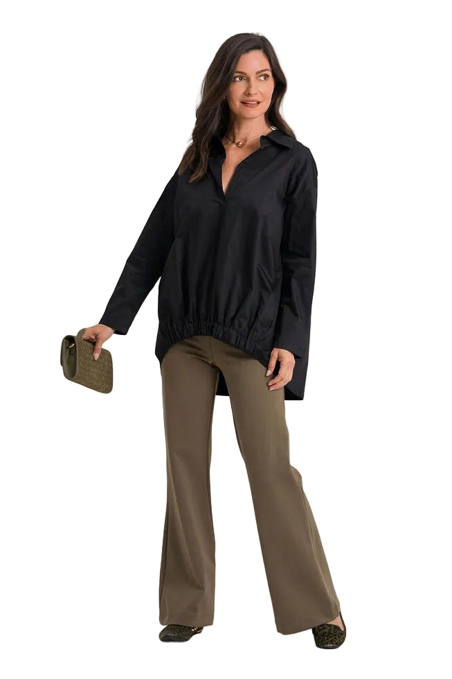 A woman modeling a 100% cotton black long-sleeve button-up shirt and brown wide-leg pants, holding a small dark olive clutch against a plain white background.