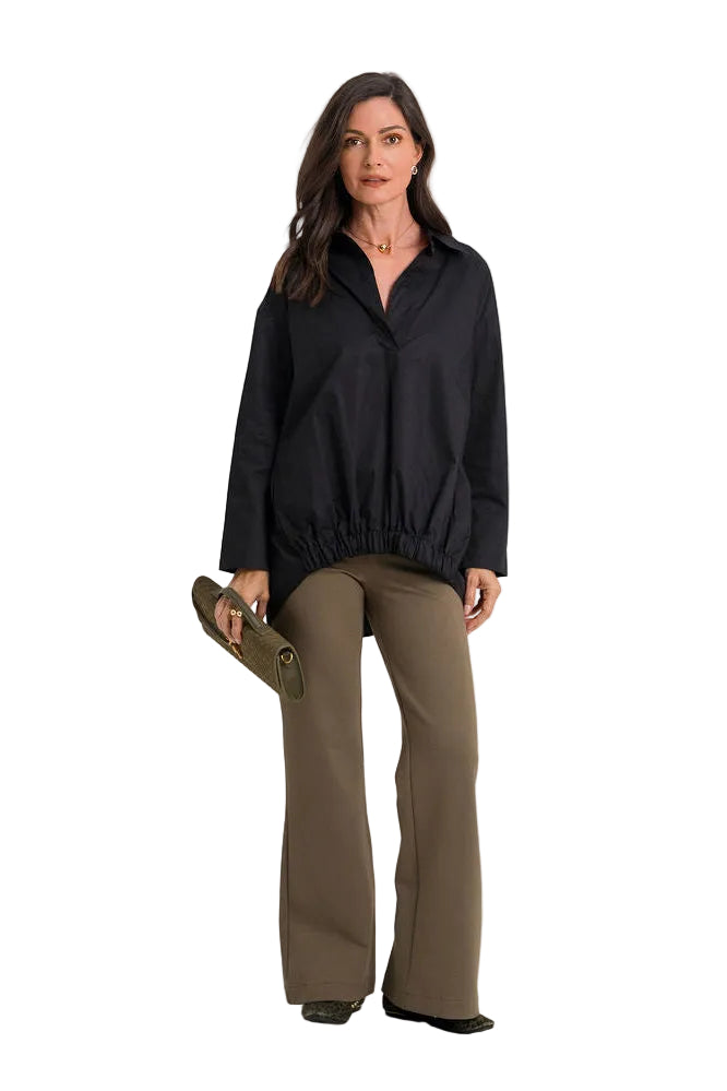 A woman modeling a 100% cotton black long-sleeve collared jacket with a gathered elastic hem, paired with olive green wide-leg pants, standing against a plain white studio background.