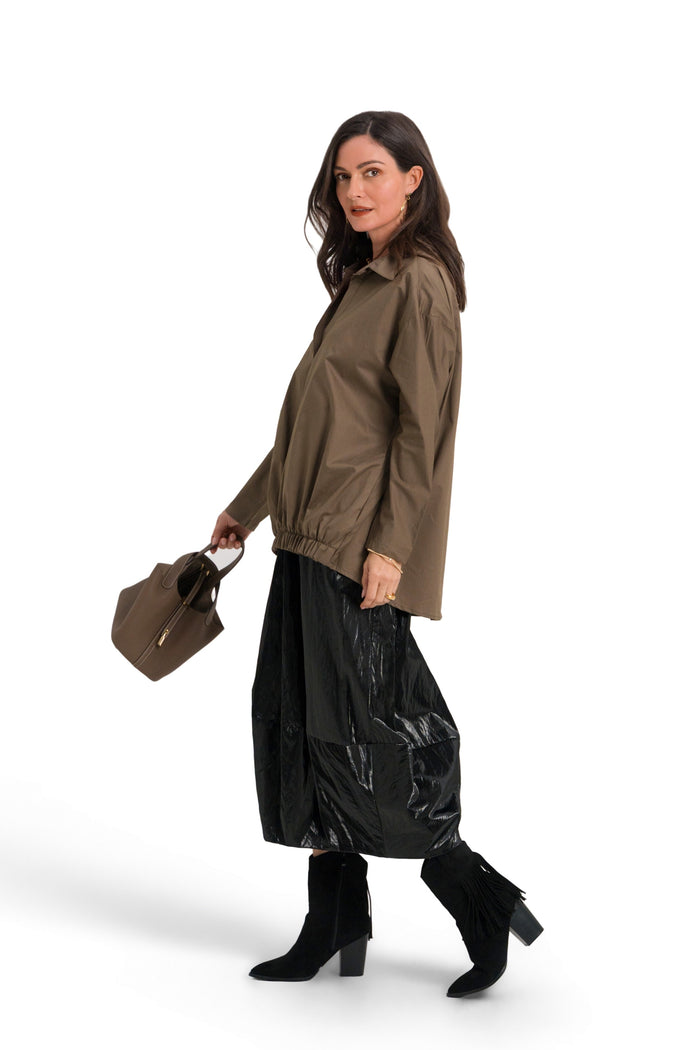 A woman modeling an 100% cotton olive green hooded jacket, black wide-leg pants, and black boots, holding a brown handbag against a solid white background.