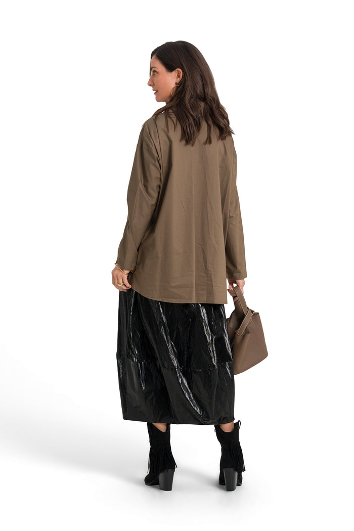 A woman is shown from the back wearing a 100% cotton brownish-olive long-sleeve top, a shiny black midi skirt, black boots, and holding a brown handbag against a solid white background.