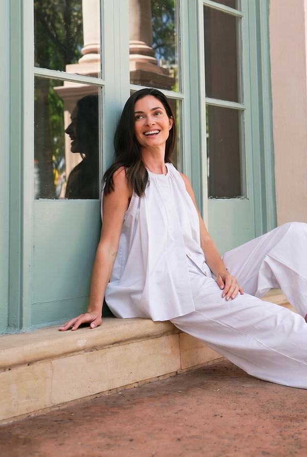 Woman in a white outfit sitting on a building ledge with large windows in the background