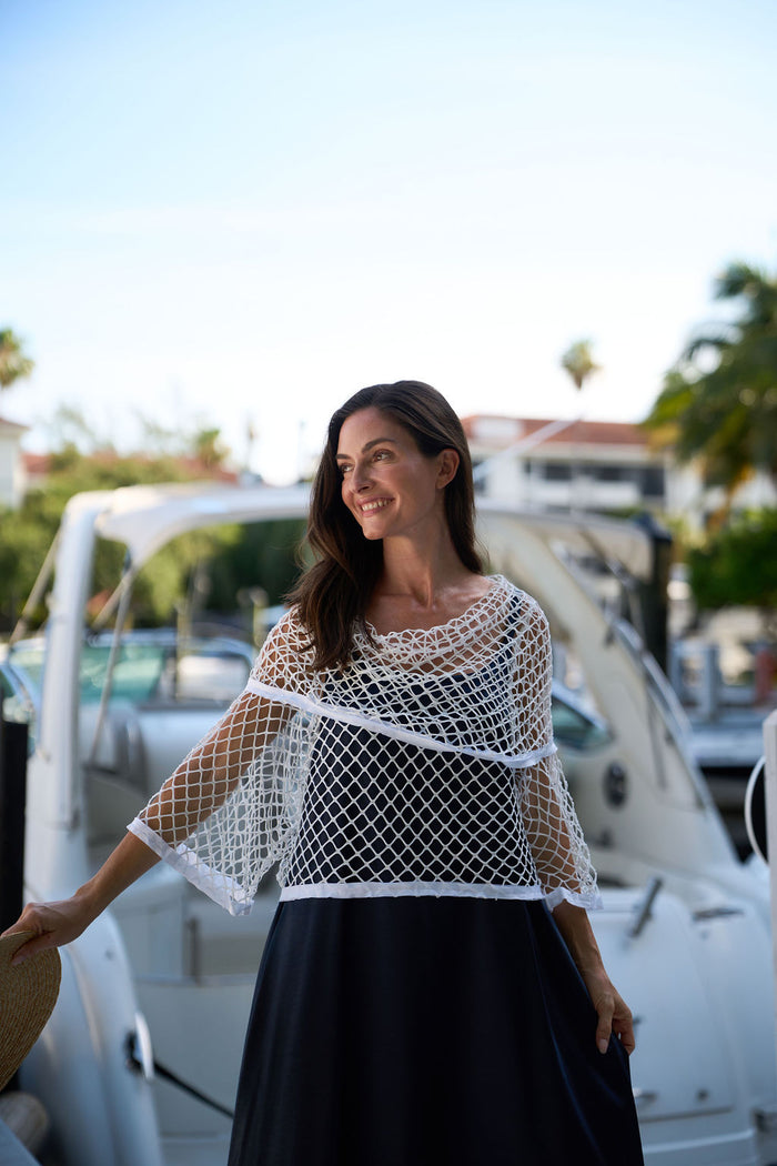 Woman wearing a white fishnet top and black skirt standing in front of a boat.