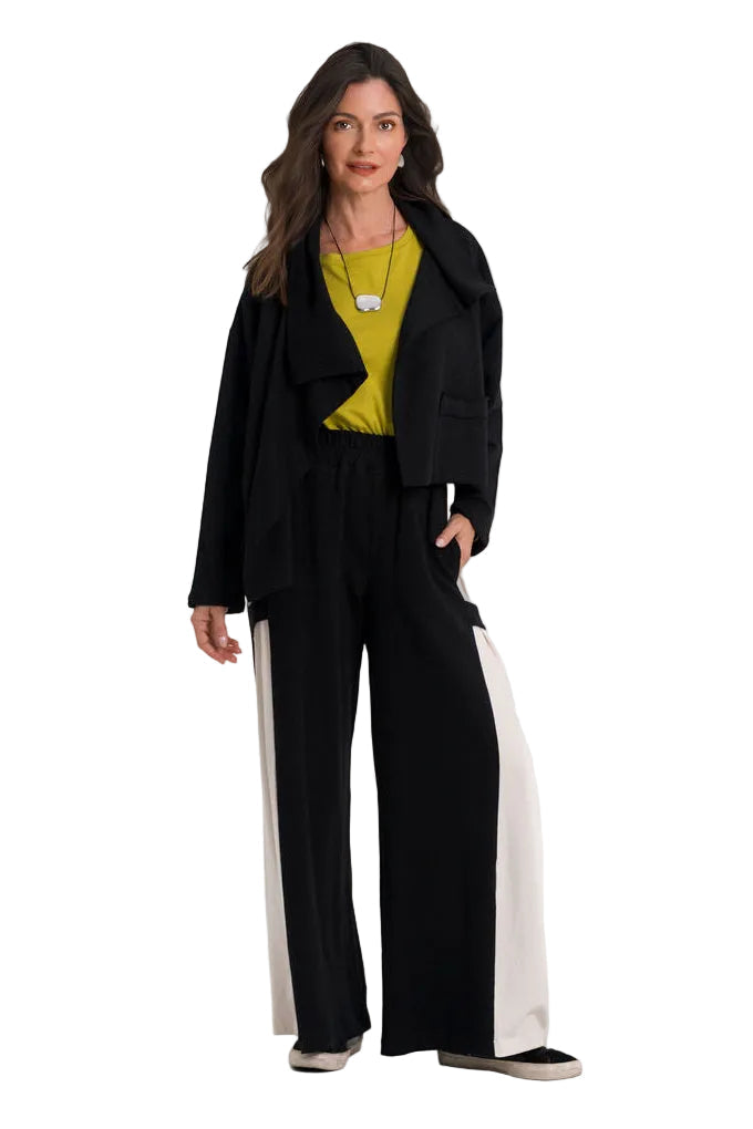 A woman modeling a black wide-leg pantsuit with a 100% cotton  black blazer, worn over a bright yellow top, standing against a plain white studio background.