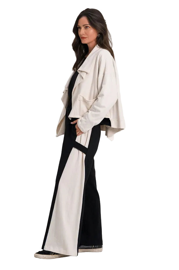 A woman models a two-tone beige and black outfit consisting of a 100% cotton wide collar jacket and matching wide-leg pants, photographed against a seamless white studio background.