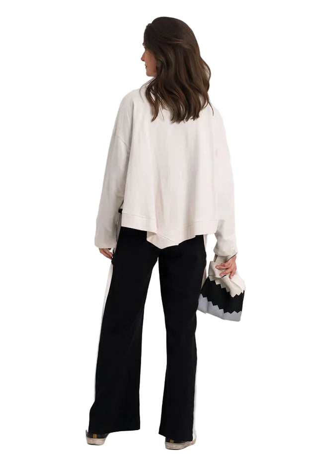 A woman shown from the back wearing a 100% cotton cream-colored long-sleeve top and black wide-leg pants, holding a black and white patterned handbag against a plain white studio background.