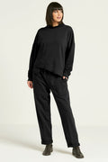 A person standing against a white background, wearing black French Terry luxury sweatpants with a drawstring closure and pockets, paired with a black top and gray shoes.