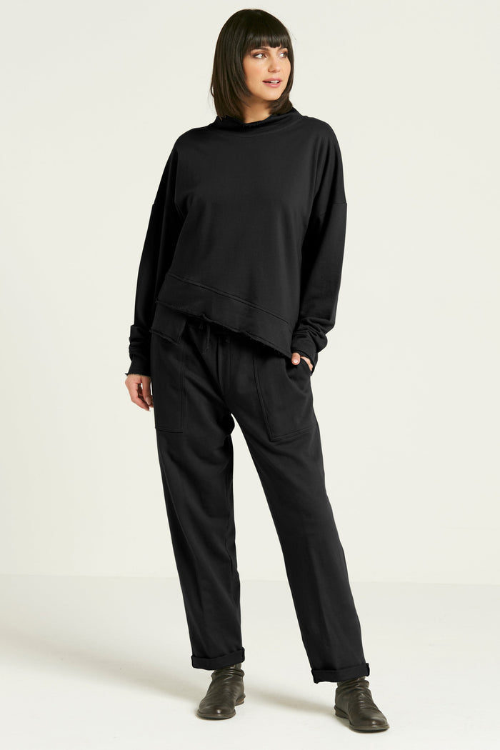A person standing against a white background, wearing black French Terry luxury sweatpants with a drawstring closure and pockets, paired with a black top and gray shoes.
