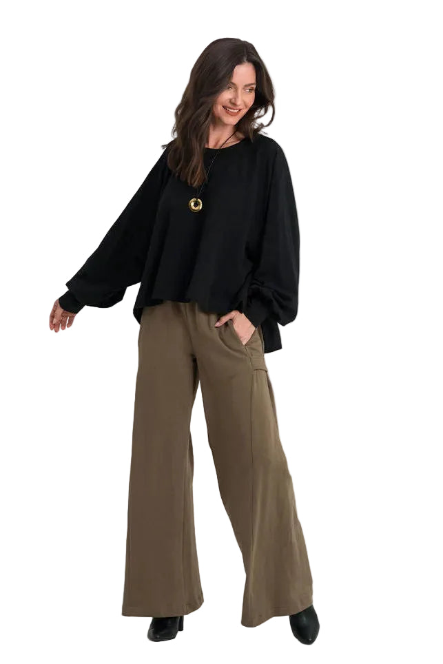 A woman modeling a 100% cotton black long-sleeve top and wide-leg olive brown trousers against a plain white studio background.