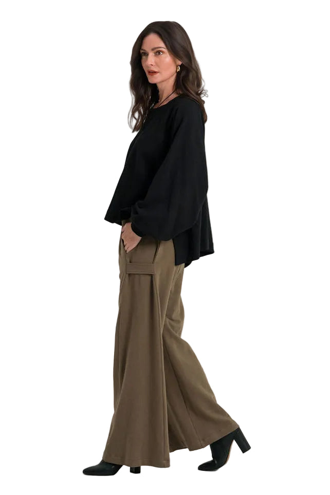 A woman modeling a 100% cotton black long-sleeve top and wide-leg olive green trousers, standing in profile against a plain white studio background.