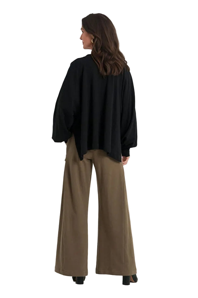 A woman is shown from the back wearing a loose 100% cotton black long-sleeve top and wide-leg brown pants against a plain white studio background.