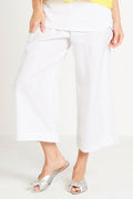 Person wearing white linen pants and silver shoes on a plain background