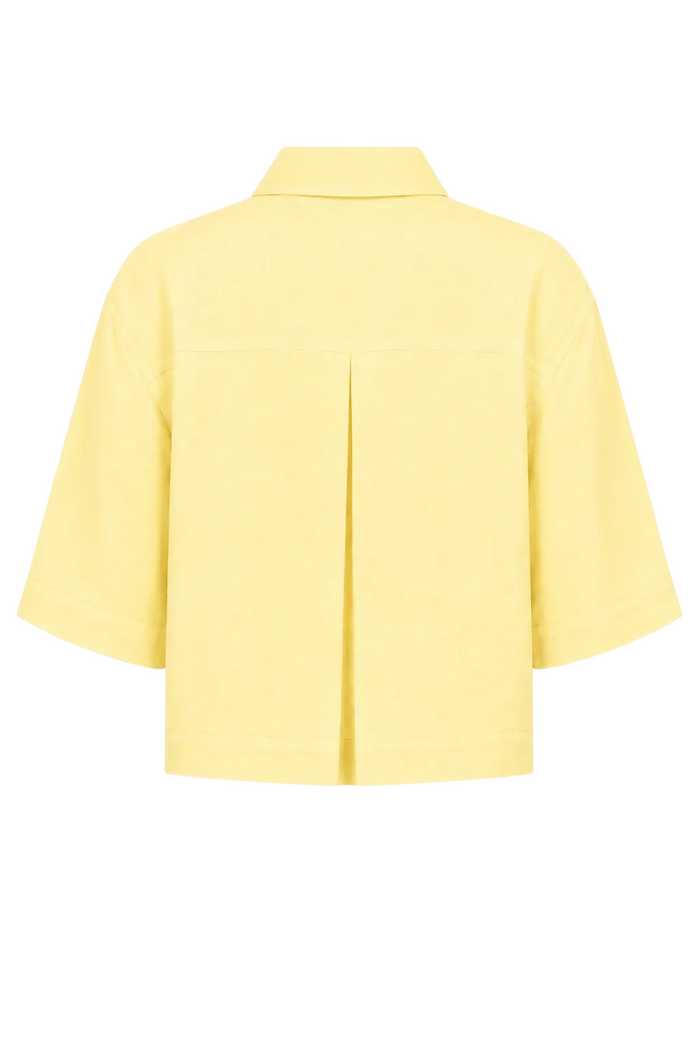 A 100% linen pale yellow short-sleeve collared shirt shown from the back, featuring a central vertical pleat, on a solid white background.
