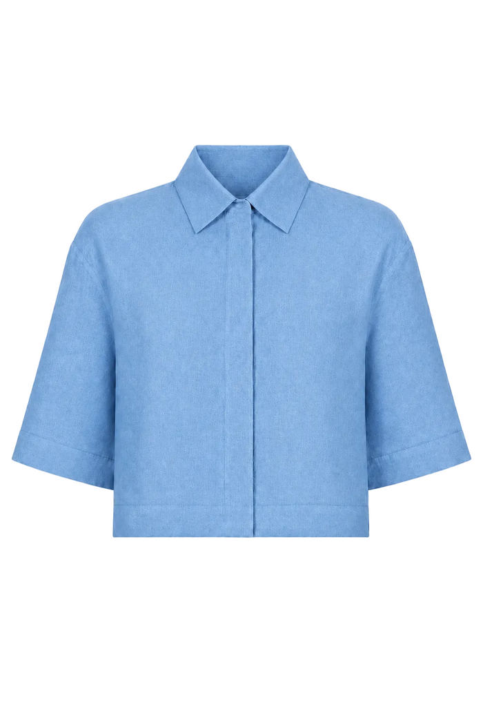 A 100% linen light blue short-sleeve collared shirt jacket with a buttonless front closure, displayed on a clean white background.