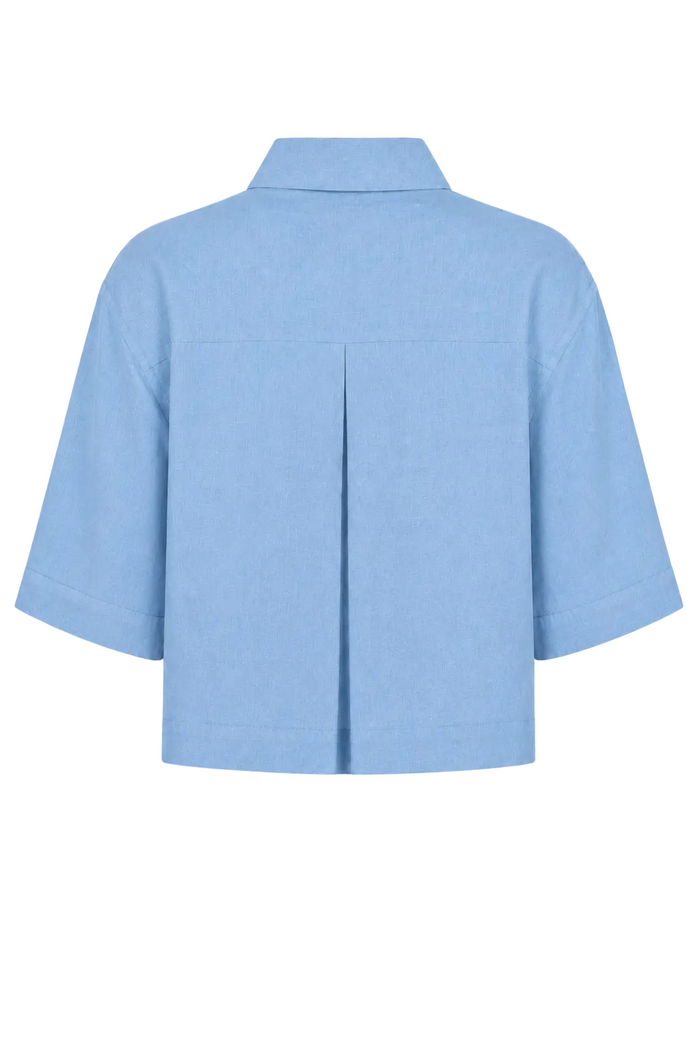 A 100% linen light blue short-sleeve cropped shirt shown from the back, featuring a central vertical pleat and a pointed collar, set against a plain white background.