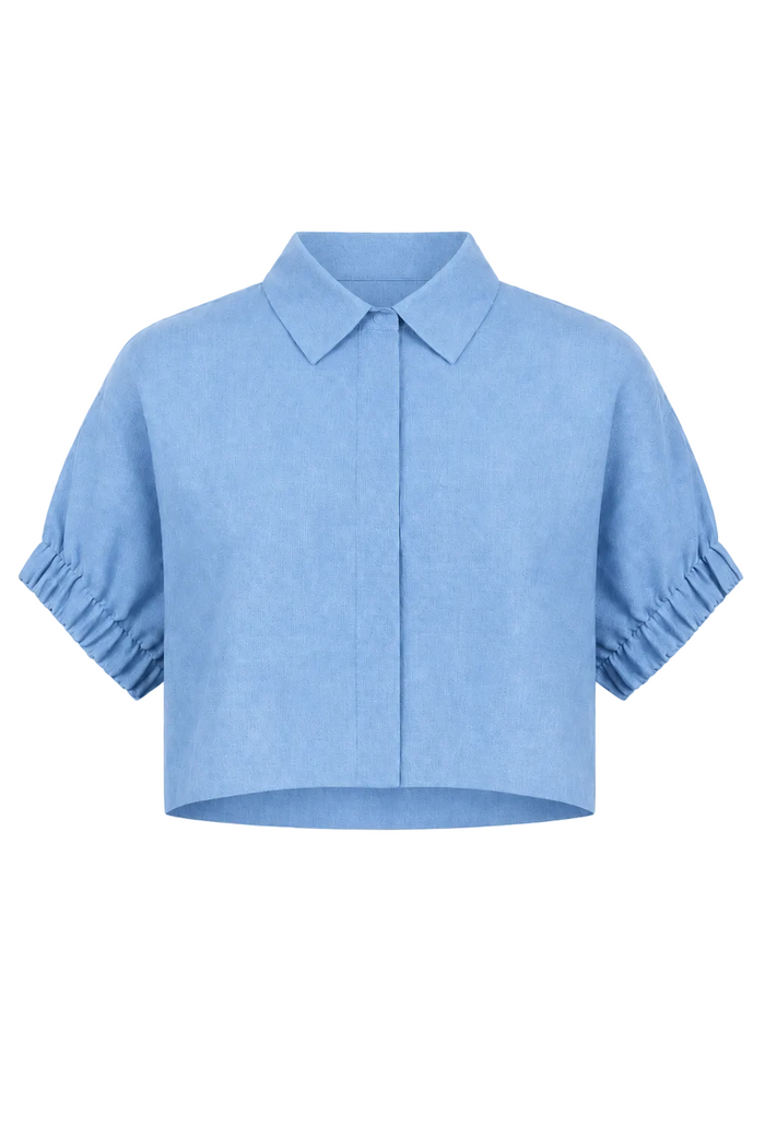 A 100% linen light blue cropped short-sleeve blouse with a pointed collar, front button placket, and gathered ruffled cuffs, shown on a plain white background.