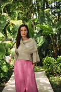 A woman stands on a garden path wearing a draped light beige top and bright pink 100% linen wide-leg pants, surrounded by lush tropical green foliage.