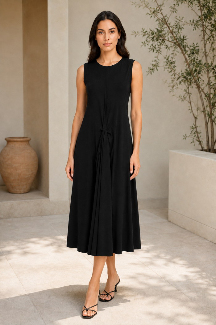 Woman wearing a black sleeveless dress standing in a minimalistic indoor setting.