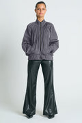 A model wearing a gray nylon bomber jacket with ruched details and a gathered neckline, paired with black wide-leg pants.