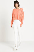 Woman wearing a peach pima cotton sweater and white pants on a plain background