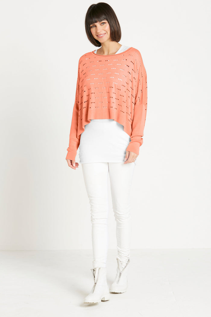 Woman wearing a peach pima cotton sweater and white pants on a plain background