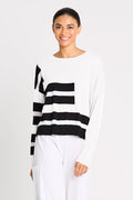Woman wearing a pink and black pima cotton striped sweater with white pants on a white background