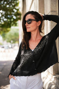 Woman wearing a black cardigan with white details and sunglasses, standing outdoors.