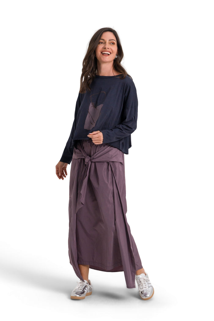 A woman modeling a 100% pima cotton dark navy blue long-sleeve top and a dusty purple wrap skirt, standing against a solid white background.