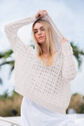 Woman wearing a light beige crochet pima cotton sweater with a hood against a blurred natural background