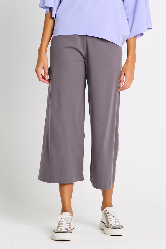 Person wearing gray pima cotton wide-leg flooded pants and a light purple top on a white background