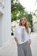 Woman wearing a white pima cotton shirt with black dot pattern and striped pants on a city street.