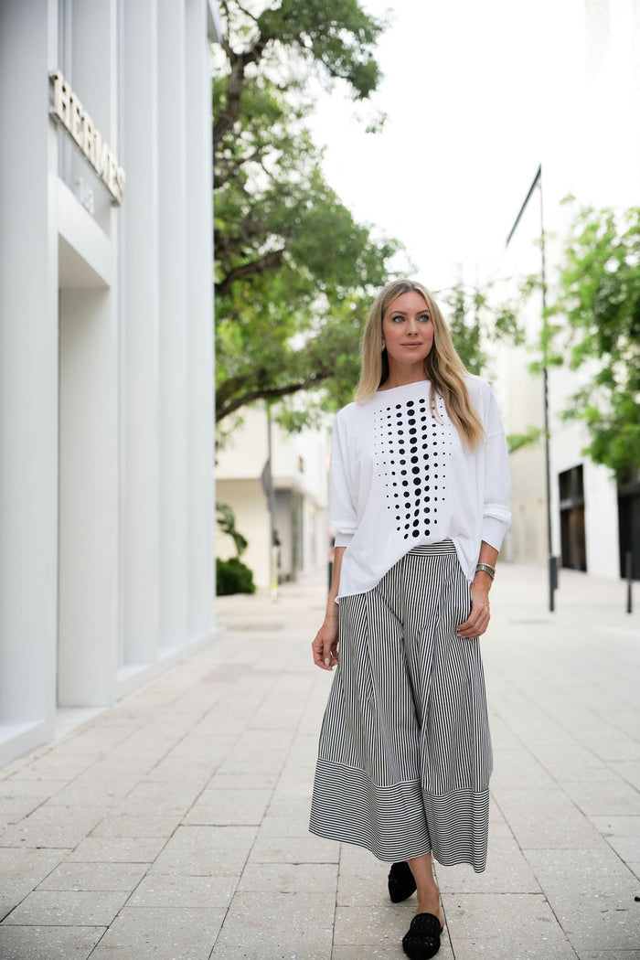 Woman wearing a white pima cotton shirt with a black geometric pattern and gray striped pants on a city street.