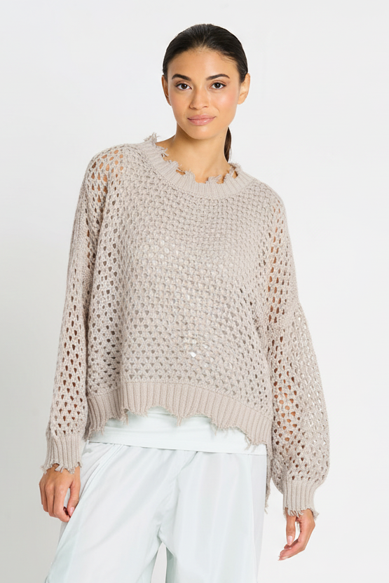 Woman wearing a beige pima cotton knit sweater and light blue pants on a white background