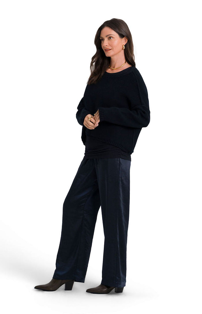 A woman modeling a black long-sleeve pima cotton knit top and matching black wide-leg trousers against a plain white studio background.