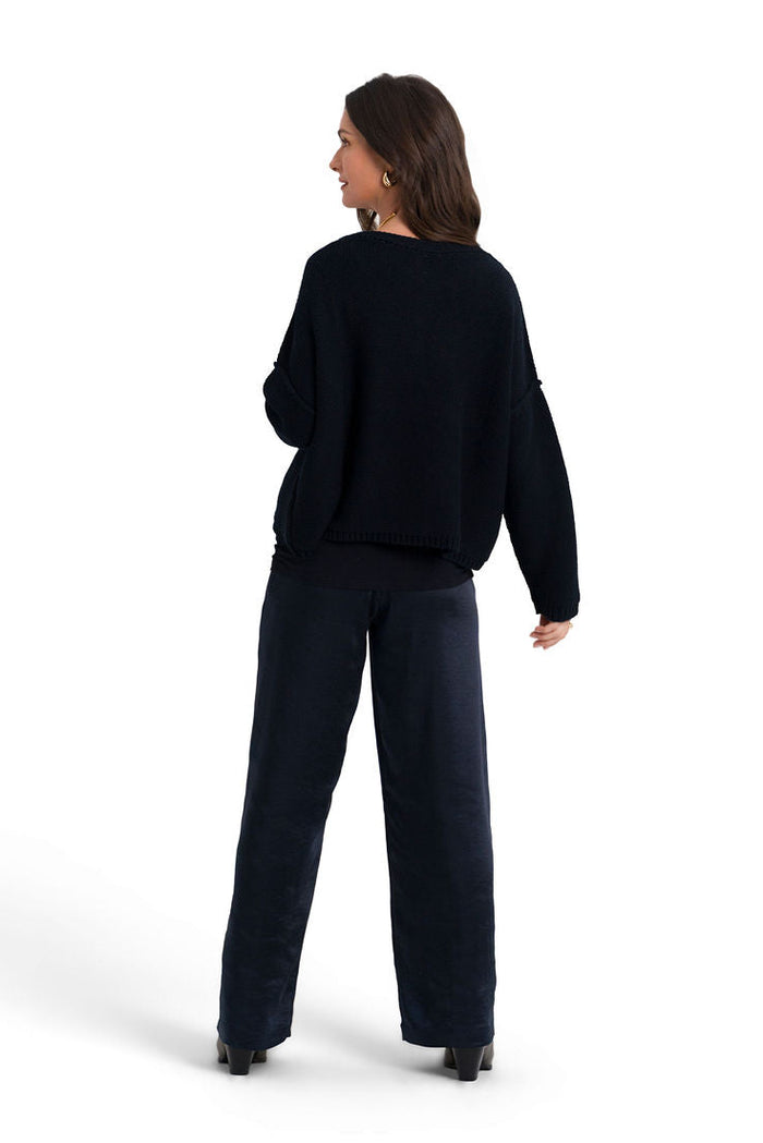 A woman is shown from the back wearing a dark navy blue knit sweater and matching wide-leg trousers against a solid white background.
