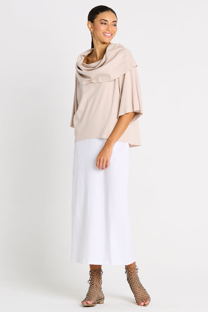 Woman wearing a beige pima cotton jackie o tee and white pants on a white background