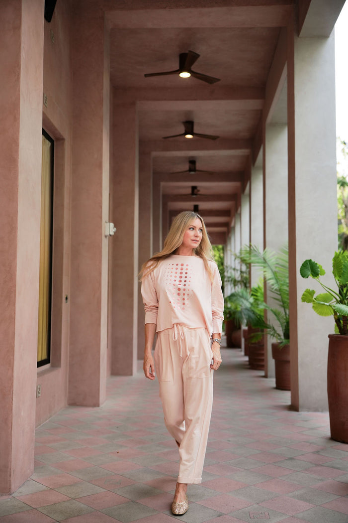 Woman walking down a long, sunlit hallway with columns and potted plants wearing a pink pima cotton boxy t-shirt.