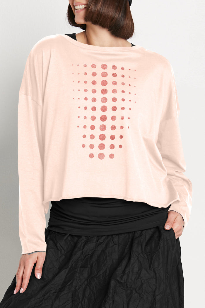Person wearing a light pink long-sleeve pima cotton boxy t-shirt with a pattern and black pants on a plain background.