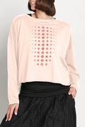 Person wearing a light pink long-sleeve pima cotton boxy t-shirt with a pattern and black pants on a plain background.