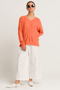 Woman wearing an orange sweater and white pants on a plain background