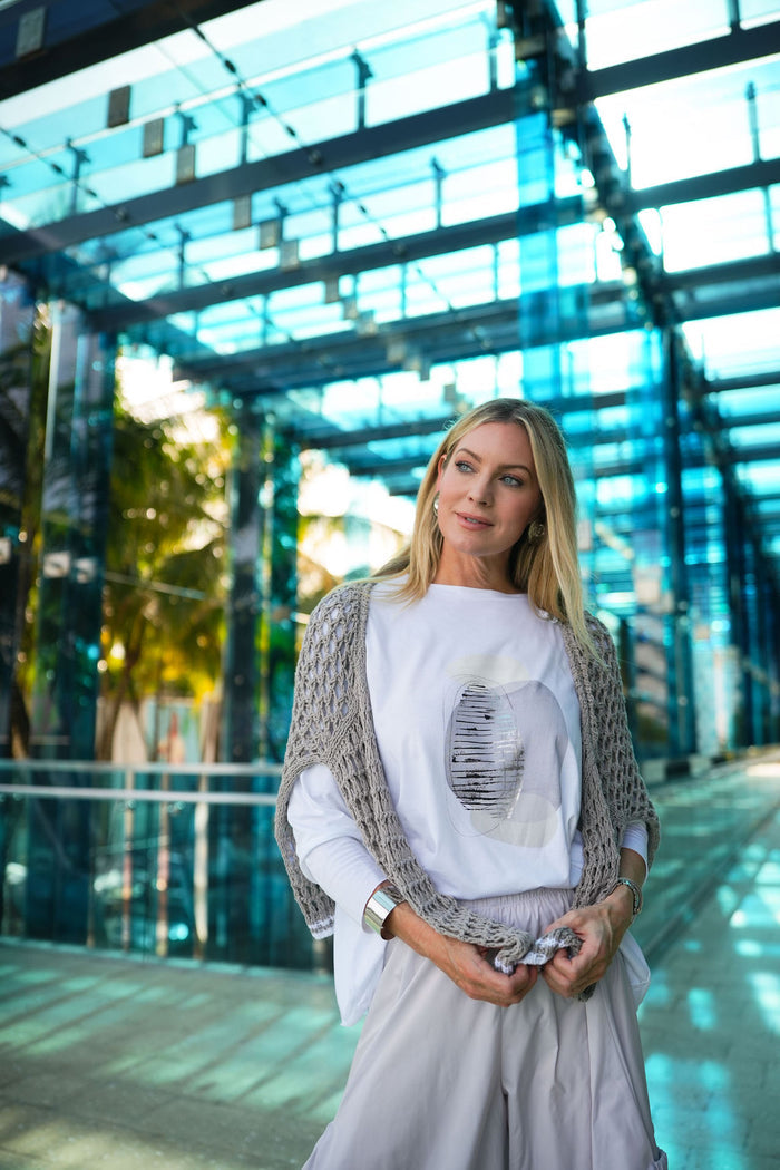 Woman standing in front of a modern glass building wearing a PLANET Pima cotton boxy t-shirt with grey graphics.