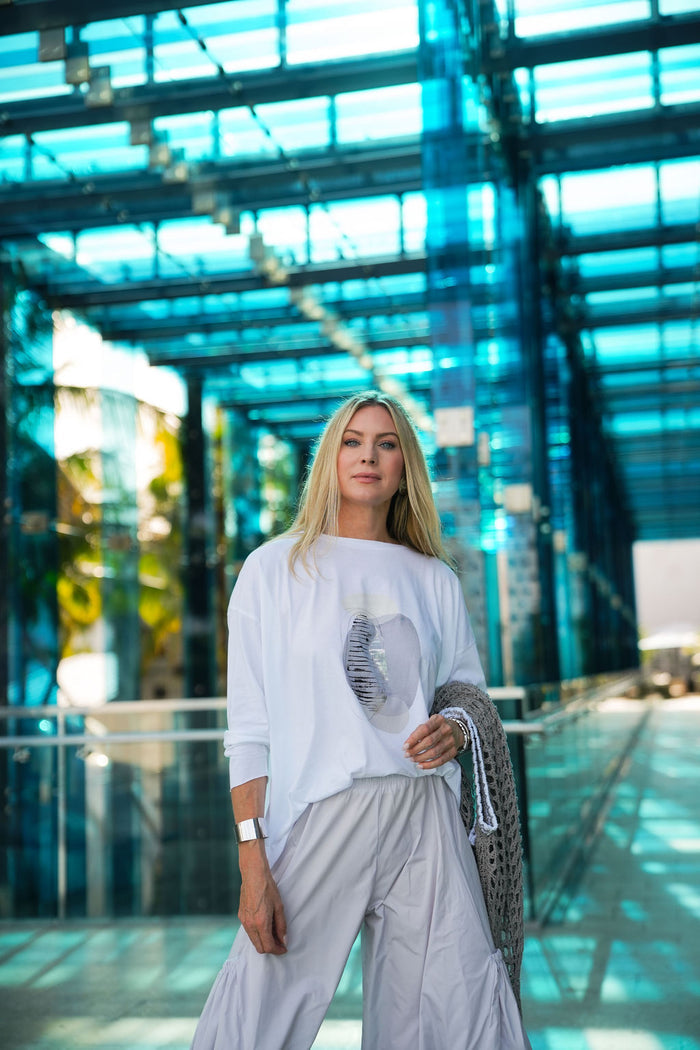 Woman in a white pima cotton boxy t-shirt standing in a modern building with glass walls.