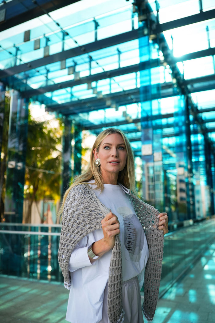 Woman wearing a gray shawl and white pima cotton boxy t-shirt in front of a modern glass building