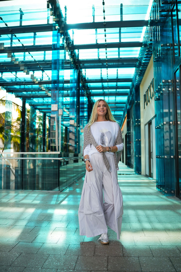Woman in a white pima cotton boxy t-shirt standing in a modern architectural setting with glass walls.